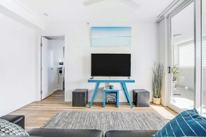 Un soggiorno moderno con una TV a schermo piatto su un supporto blu, un divano, un tappeto decorato e una pianta in vaso.