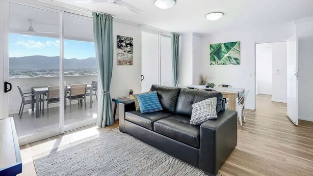 Ein modernes Wohnzimmer mit einer schwarzen Ledersofa, einem Essbereich mit Tisch und Stühlen und einer großen Schiebeglasdoor zu einem Balkon.