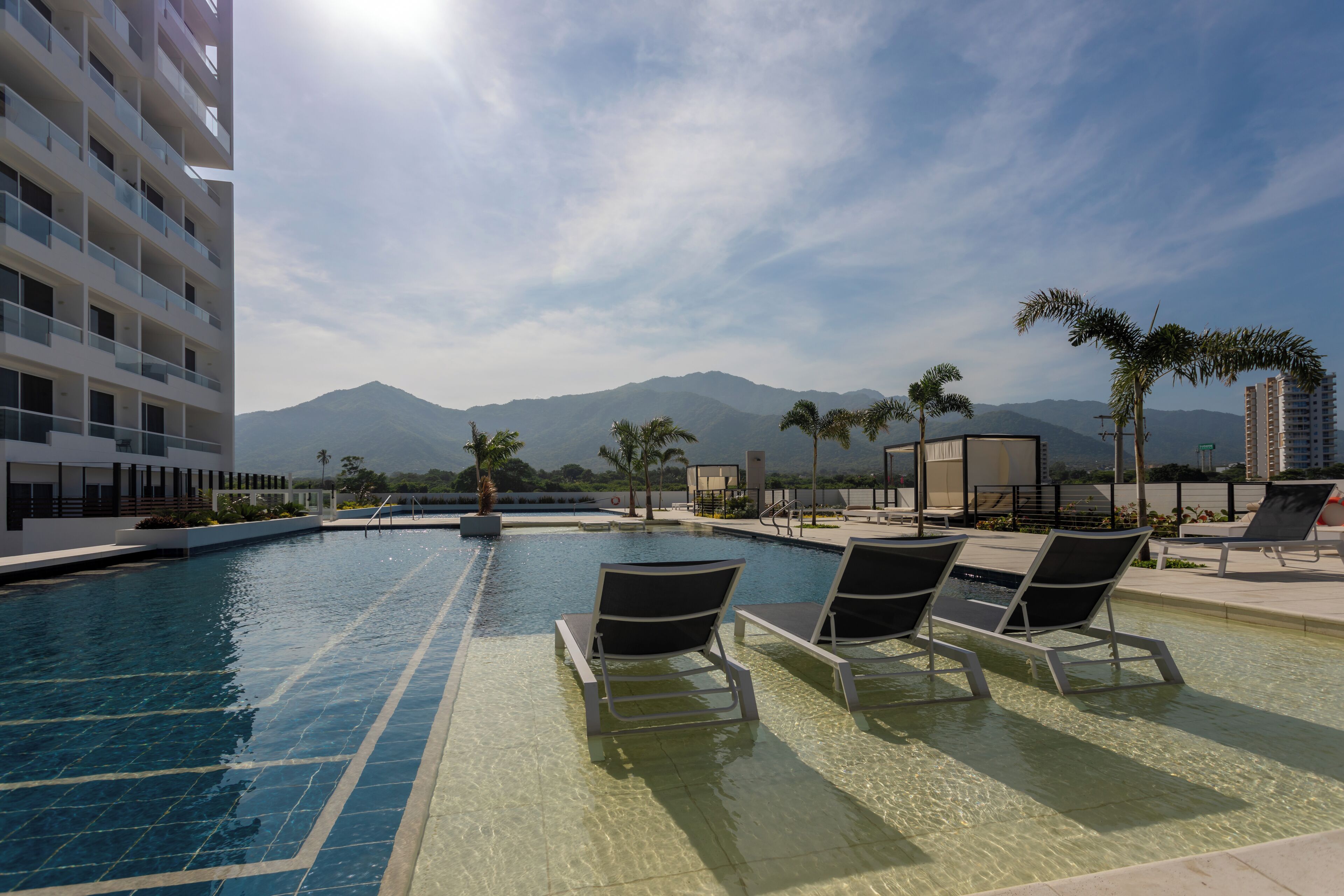 A pool area with lounge chairs, a clear sky, and mountains in the background.