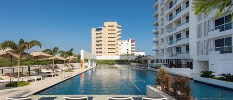 A swimming pool with lounge chairs and palm trees, surrounded by modern buildings.