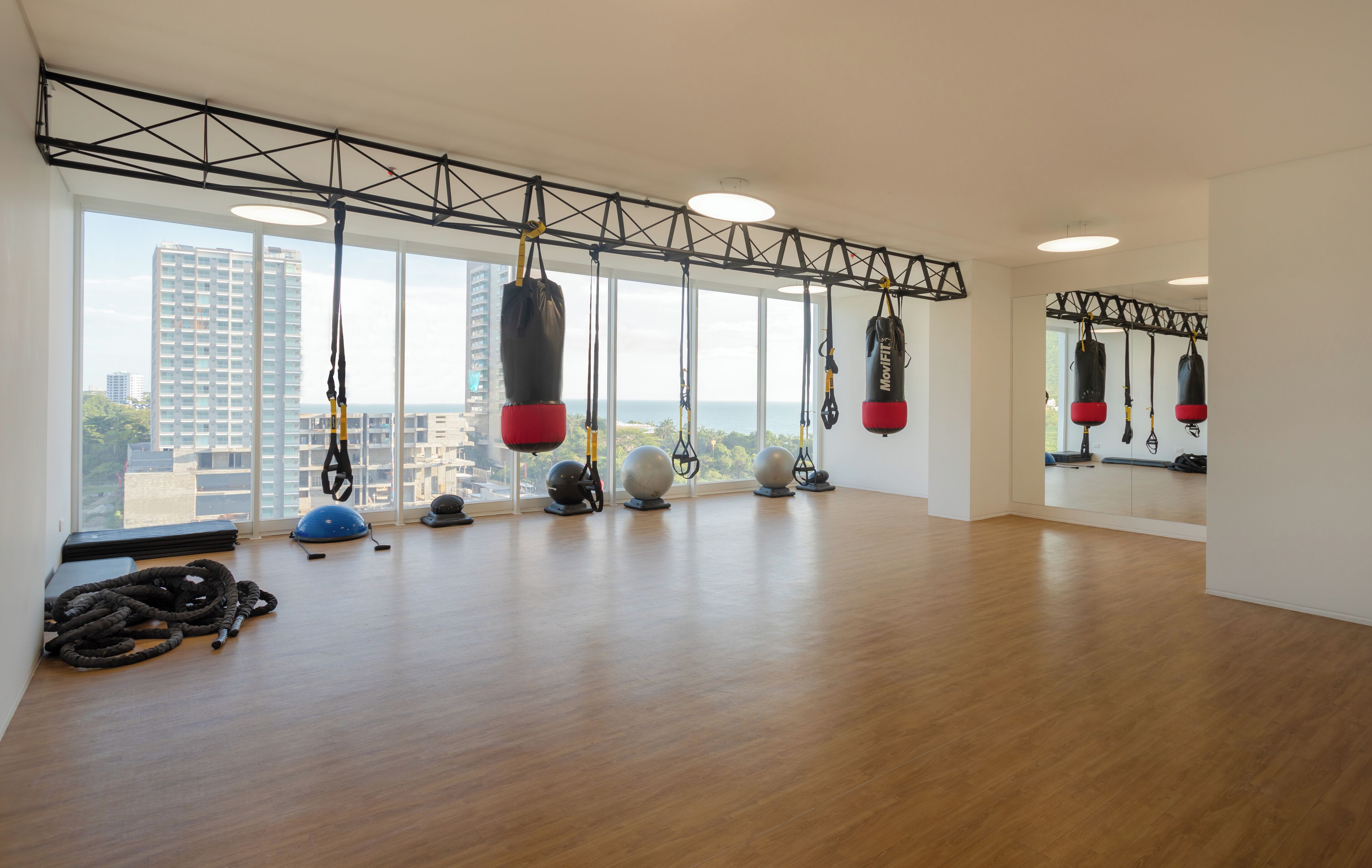 Ett rymligt gym med stora fönster, olika typer av träningsutrustning och utsikt över staden.