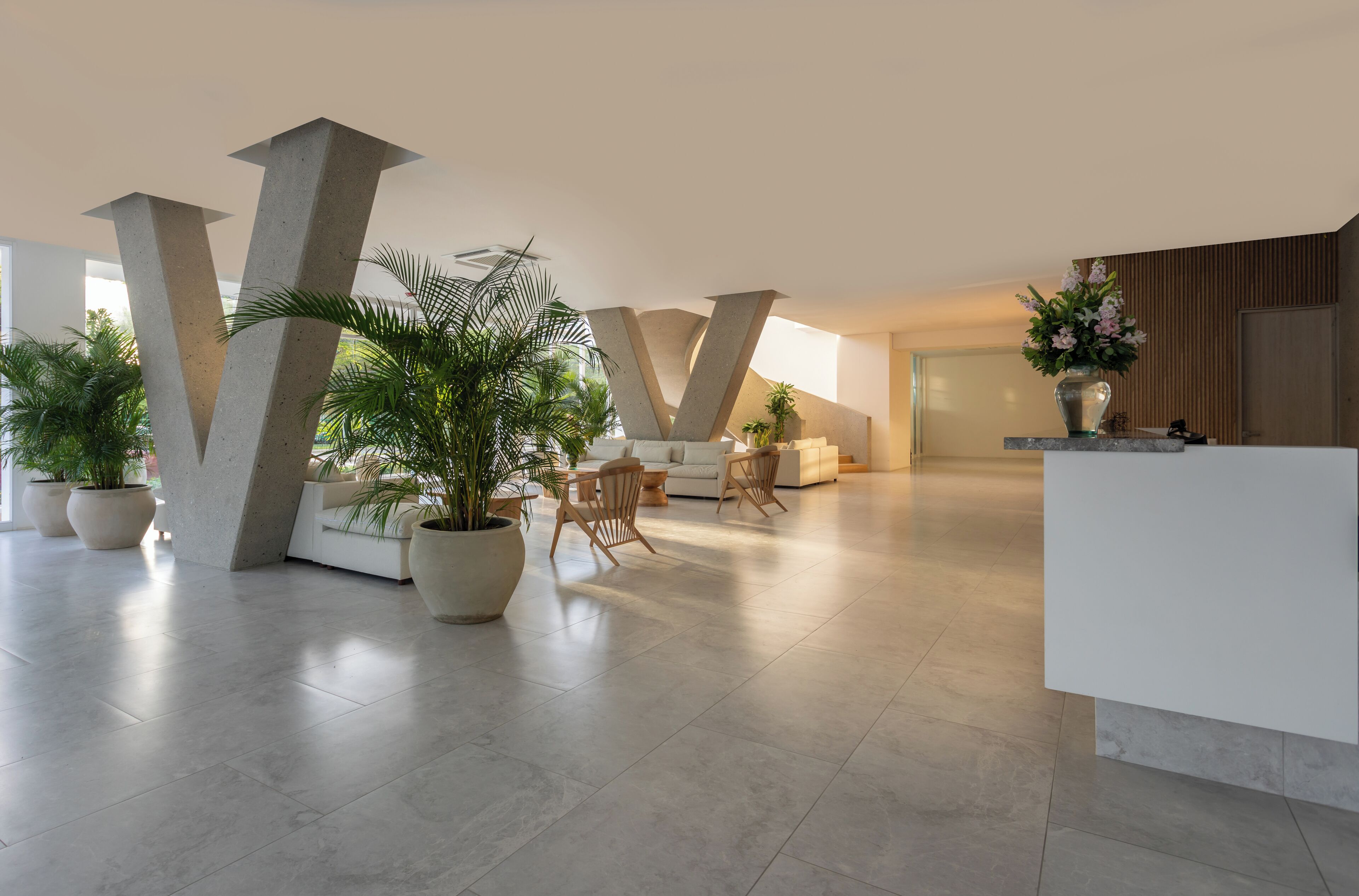 Un vestíbulo amplio con un diseño moderno, que incluye una recepción, zona de estar con sillones y plantas en macetas grandes.