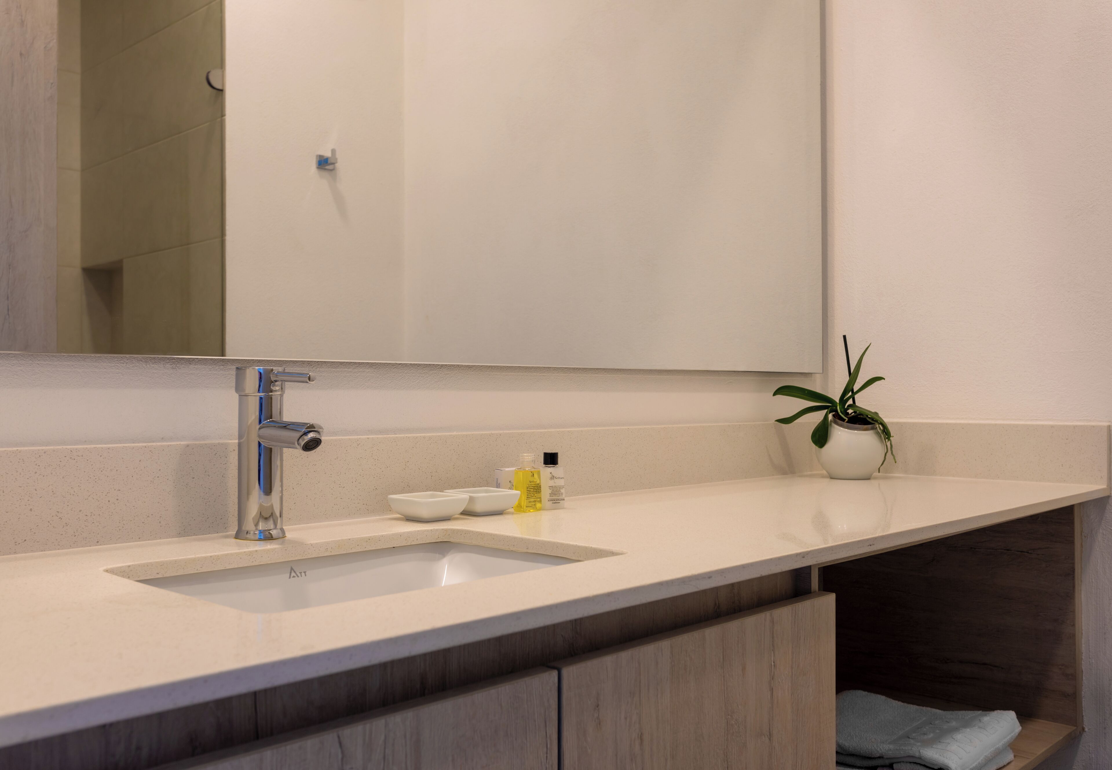 A modern bathroom with a large mirror, a sink, and a potted plant.