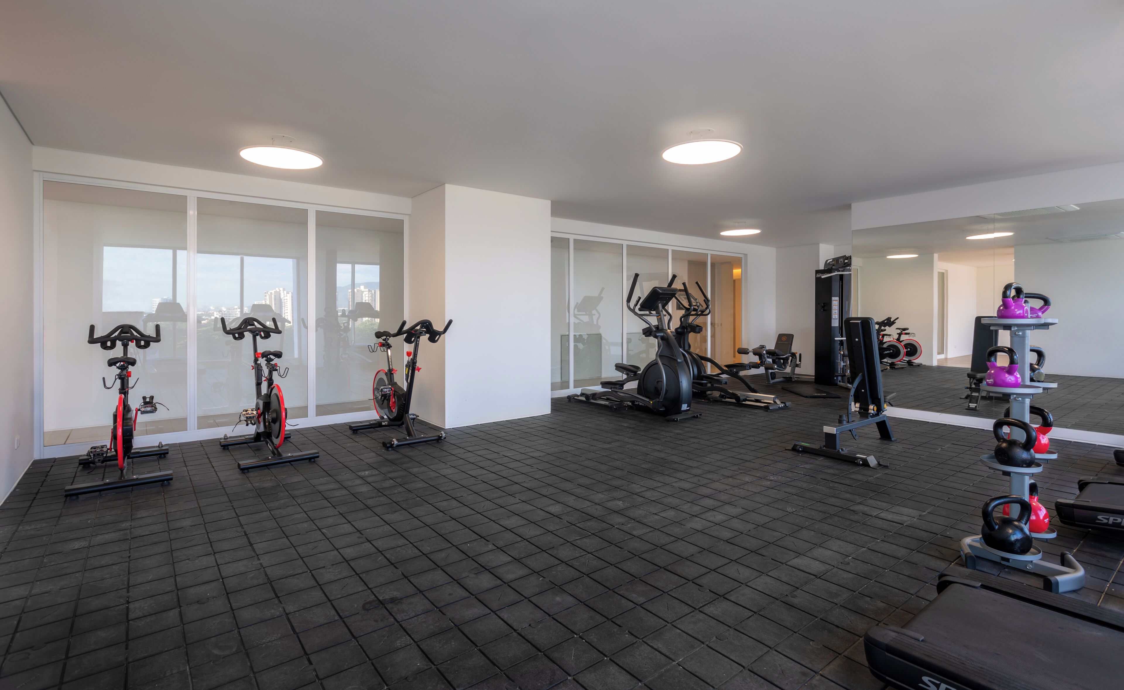 Ein Fitnessstudio mit Trainingsgeräten, großen Fenstern und Fliesenboden.