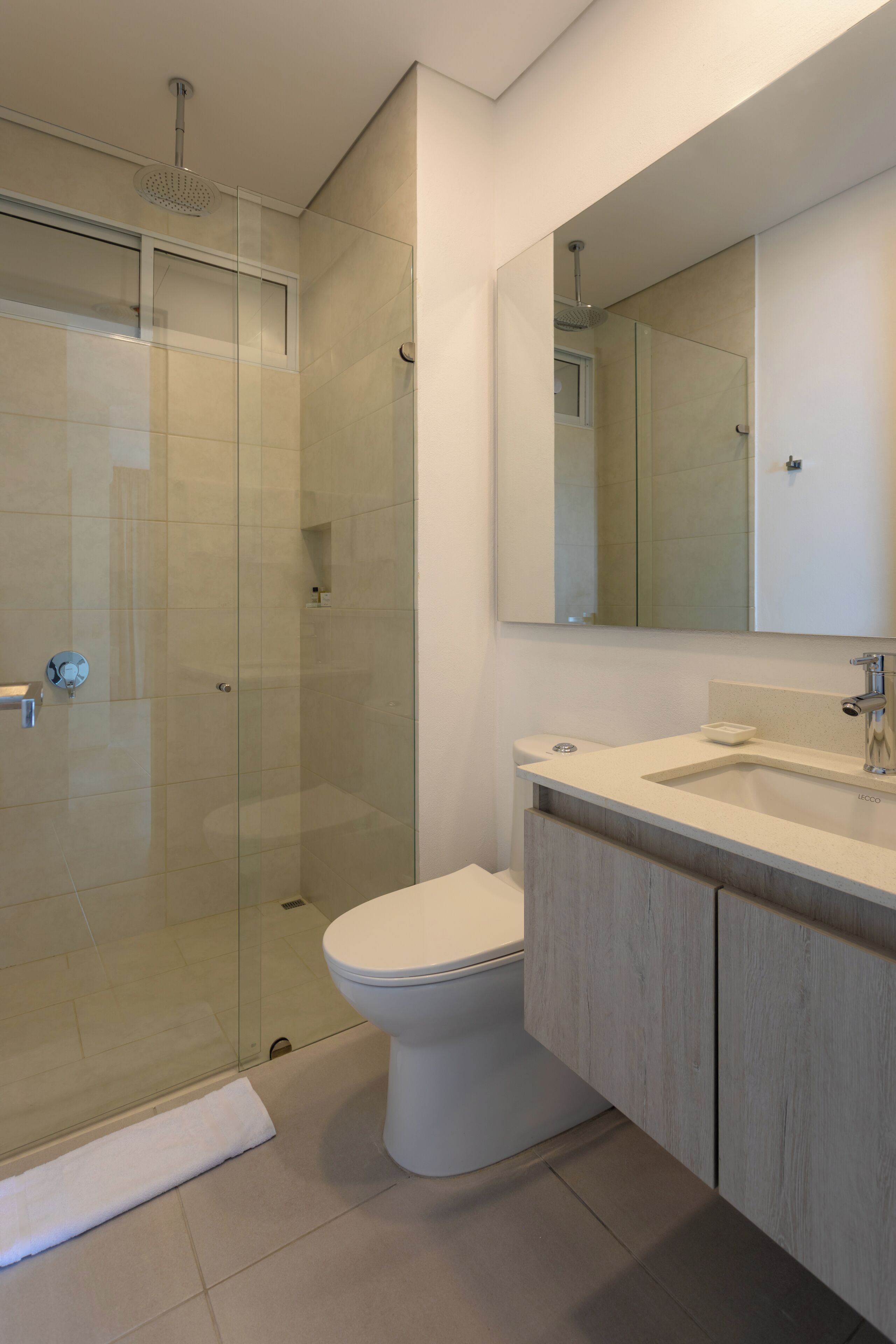 Ein modernes Badezimmer mit einer in Glas eingefassten Dusche, einer weißen Toilette und einem Waschtisch mit Spiegel.