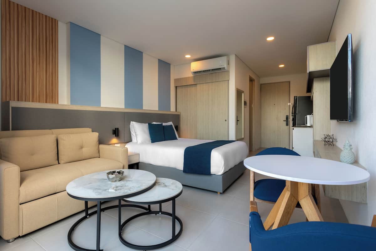 Une chambre d’hôtel moderne équipée d’un lit, d’un canapé, de deux petites tables rondes et d’un téléviseur fixé au mur.