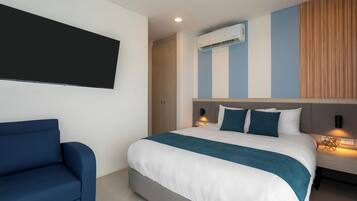 Ett modernt hotellrum med en stor säng, en blå fåtölj, en platt-TV och en luftkonditioneringsanläggning på väggen.