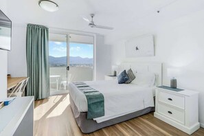 A bedroom with a bed, a nightstand, a desk, and a view of the outdoors.