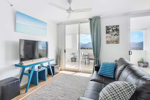 Una sala de estar con televisor, sofá, mesa de centro, ventilador de techo y puerta corrediza de vidrio que da a un balcón.