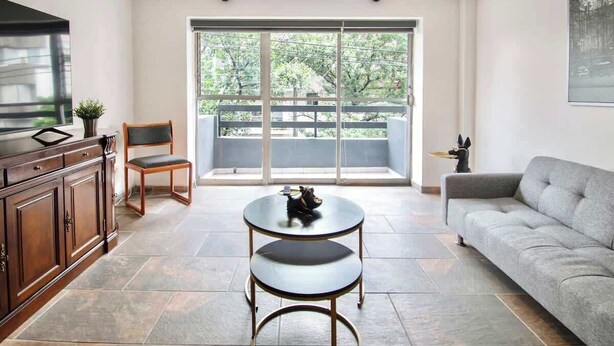 A modern living room with a sofa, a dining table with two chairs, a cabinet, and a large sliding glass door to a balcony. - Bright & Spacious 3-BR-2BTH, near WTC/ Insurgentes (Ciudad de México)