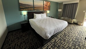 A hotel room with a large bed, two bedside lamps, a nightstand, a window with curtains, and a wall-mounted painting. - Homegate Inn And Suites Collierville TN (Collierville)