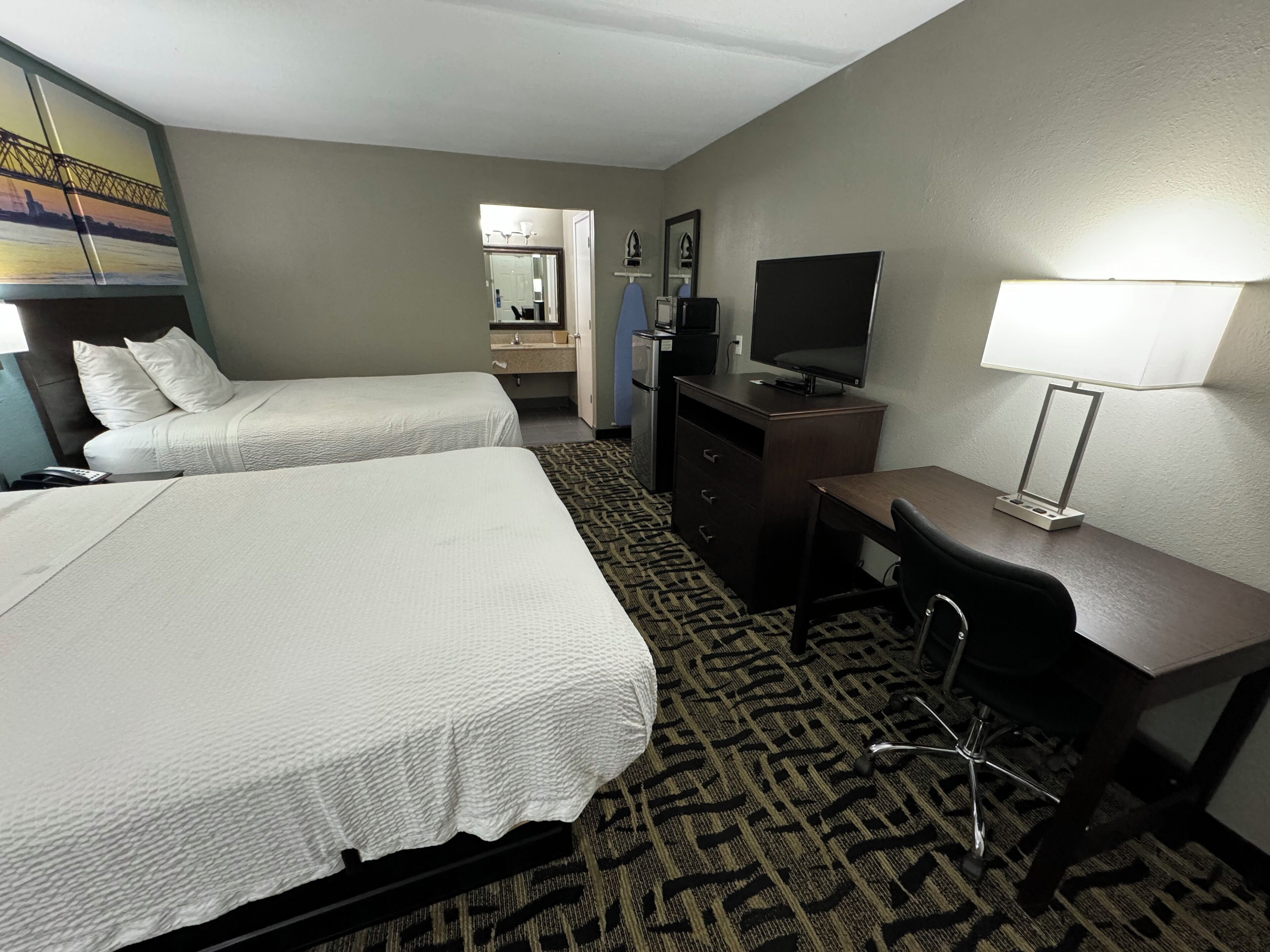 A hotel room with two beds, a desk, a television, a mirror, and a patterned carpet.