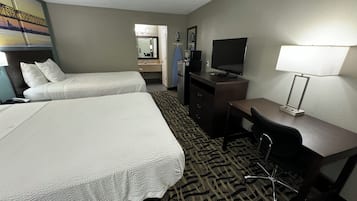 A hotel room with two beds, a desk, a television, a mirror, and a patterned carpet.