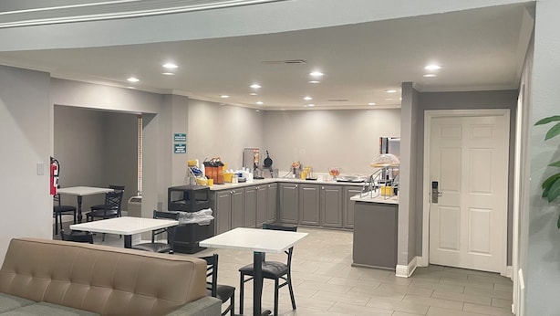 A compact kitchen with modern appliances, a dining area with a sofa, and a door leading to another room. - Homegate Inn And Suites Collierville TN (Collierville)