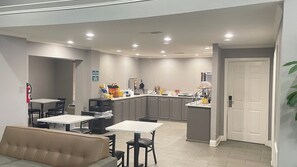 A compact kitchen with modern appliances, a dining area with a sofa, and a door leading to another room. - Homegate Inn And Suites Collierville TN (Collierville)