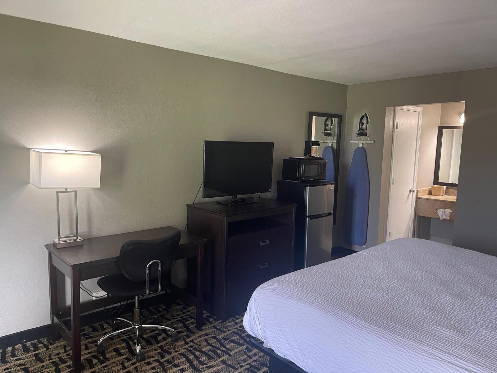 A hotel room with a bed, a desk with a computer, a television, a microwave, and a bathroom with a mirror and sink.