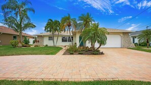 A residential house with a paved driveway, palm trees, and a stone facade.