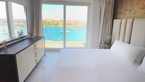 Ein Hotelzimmer mit Bett, Schminktisch, Spiegel und Blick auf das Meer und die Stadtlandschaft.