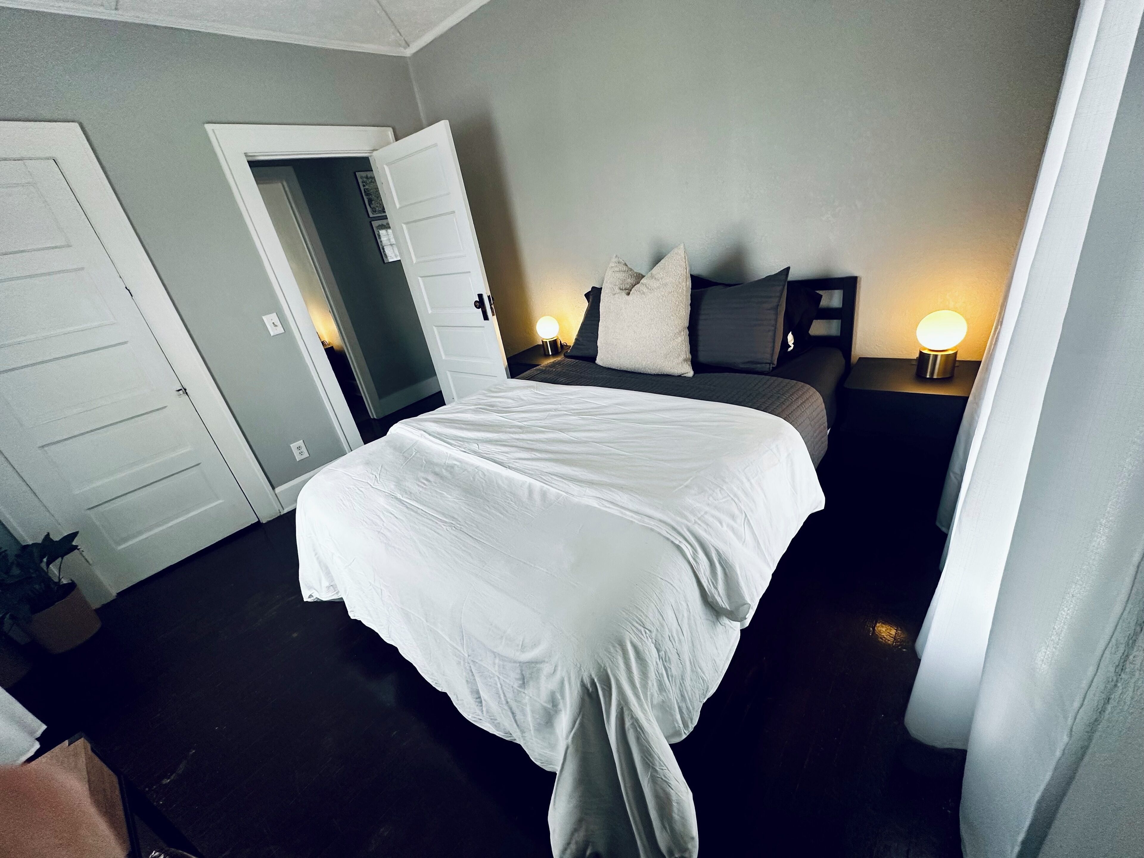 A hotel room with a large bed, two bedside tables with lamps, a door, and a dark floor.
