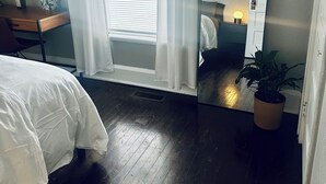 Un dormitorio con cama, escritorio, espejo, planta en maceta y ventana con cortinas.