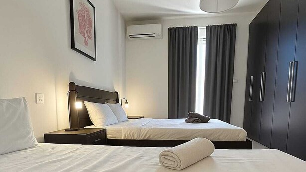 Ein Hotelzimmer mit zwei Betten, einem dunklen Kleiderschrank, einem gerahmten Bild an der Wand und einem Fenster mit Vorhängen.