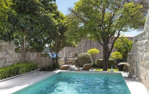 A swimming pool with lounge chairs and a stone wall in the background.