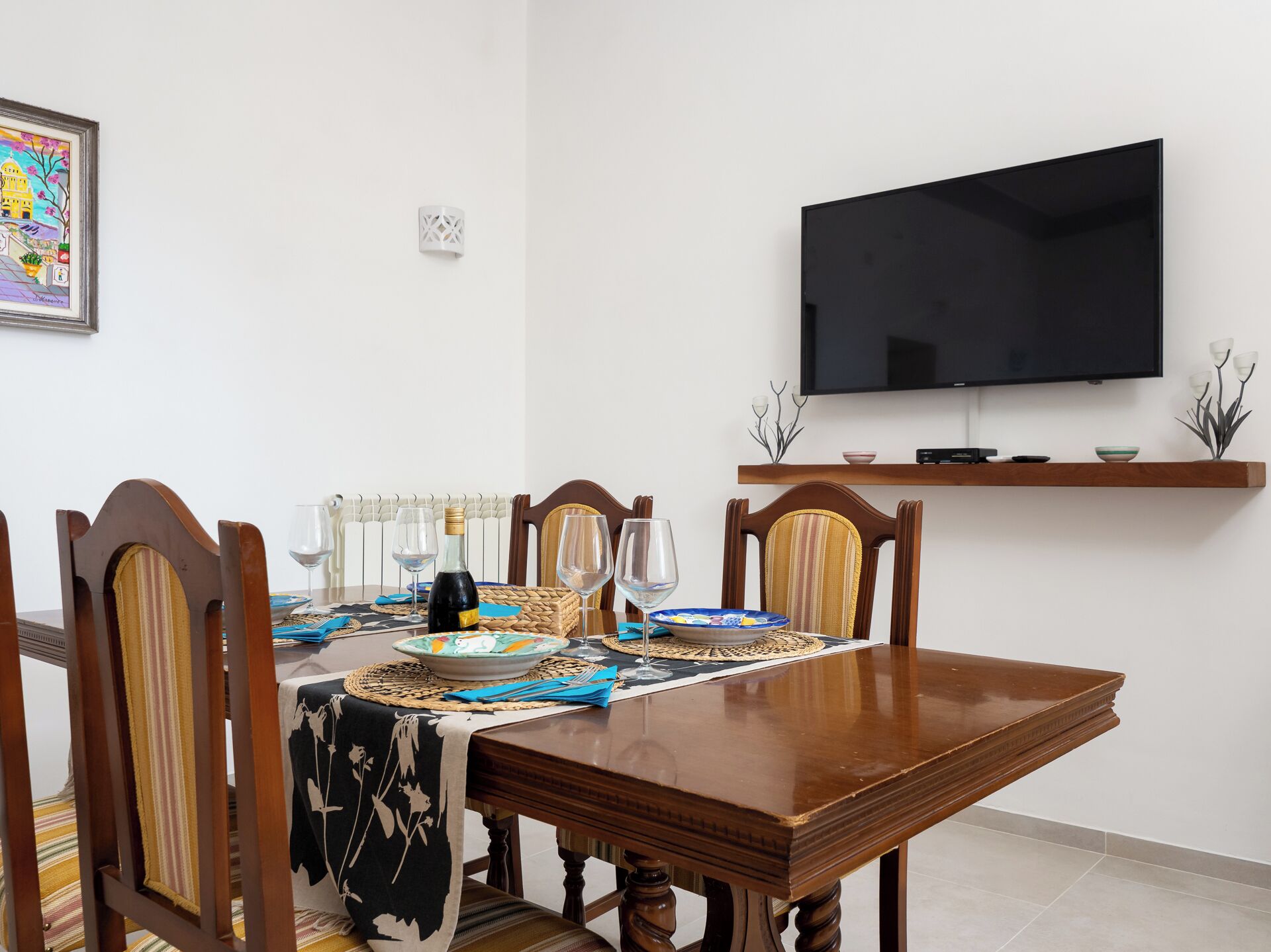 A dining area with a wooden table, chairs, and a television mounted on the wall.
