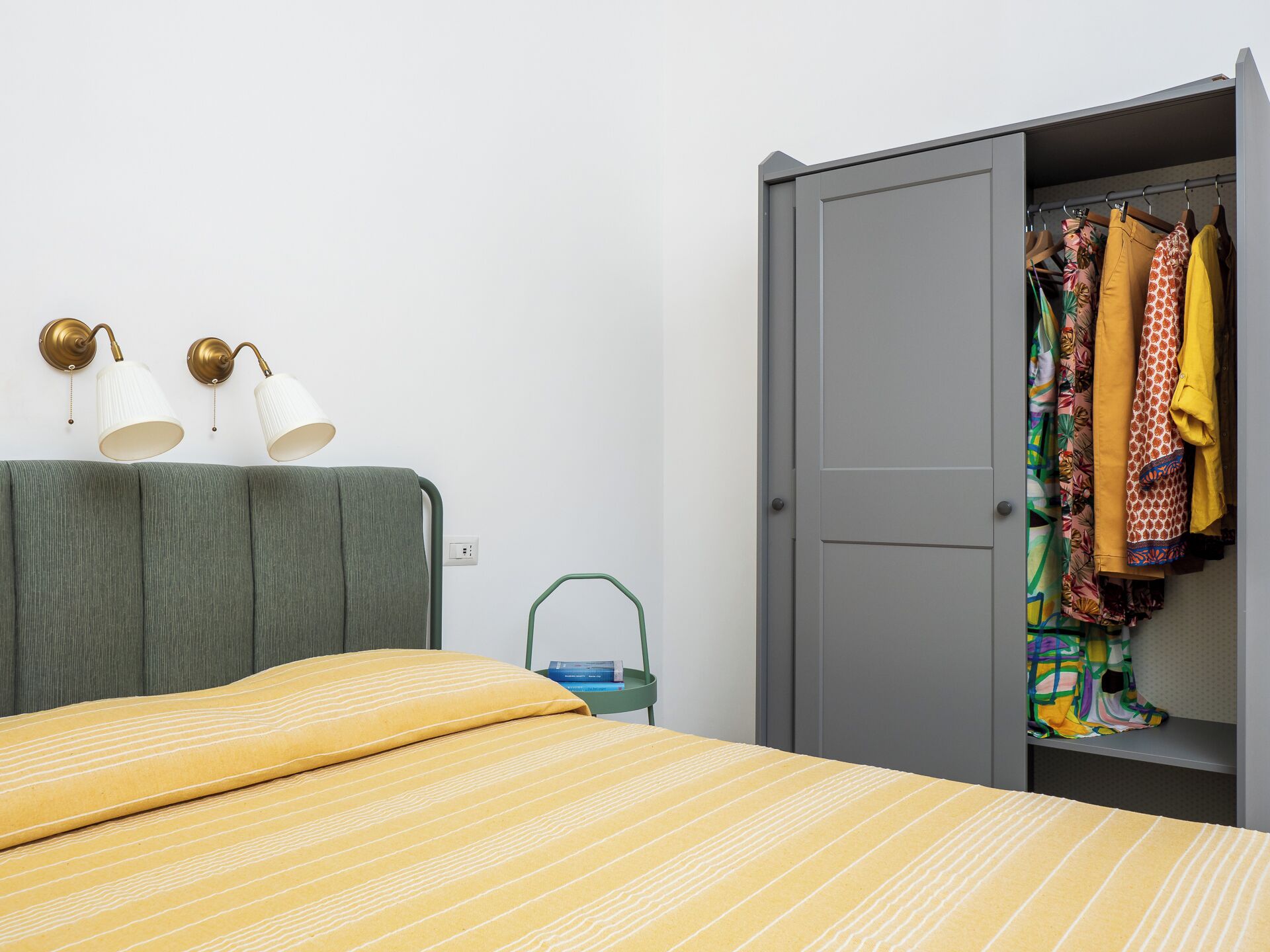 A bedroom with a bed, a wardrobe, and two wall-mounted lamps.