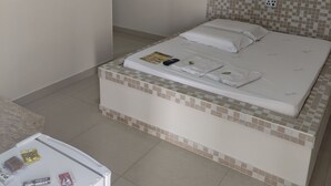 A neatly arranged bedroom with a bed, a small bedside table, and a wall-mounted shelf with decorative items. - Motel Classe A  (Limeira)