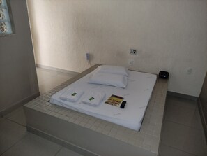 Een opgemaakt bed met witte lakens en kussens, een afstandsbediening en een brochure op het bed.