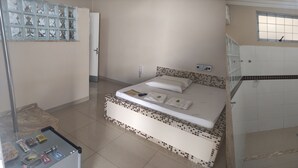 A hotel room with a bed, a small bedside table with snacks, a window, a shower area, and a toilet. - Motel Classe A  (Limeira)