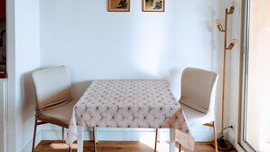 A dining area with a table and two chairs, wooden flooring, and two framed paintings on the wall.