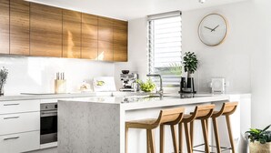 A modern kitchen with white cabinetry, a central island with bar stools, a coffee machine, and a clock on the wall.