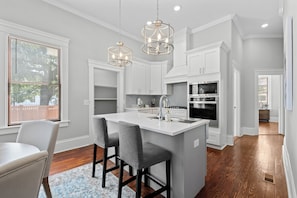 A modern kitchen with white cabinetry, a central island with bar stools, and pendant lighting.