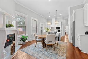 A modern kitchen with white cabinets, a wooden dining table, and a fireplace.