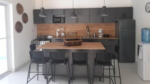 A modern kitchen with dark cabinets, a wooden island, black bar stools, and pendant lighting. - Villa Sleeps 8 With Private Pool (Sosúa)