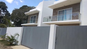 A modern two-story house with a grey fence, a balcony, and a small garden area. - Villa Sleeps 8 With Private Pool (Sosúa)
