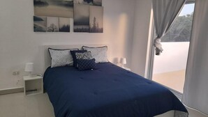 A bedroom with a large bed, a nightstand, a lamp, and a window with curtains. - Tropical Villa Escape in Sosua (Sosúa)