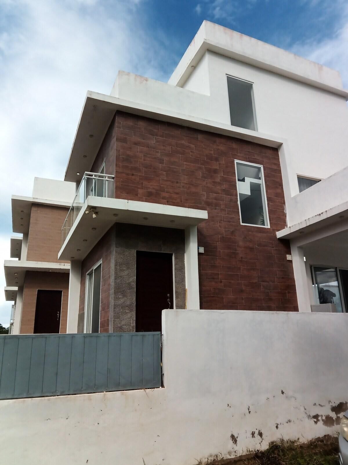 A modern multi-story residential building with a flat roof, large windows, and a balcony.