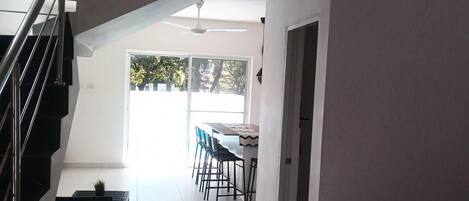 A modern interior with a staircase, a dining area with chairs and a table, and a ceiling fan.