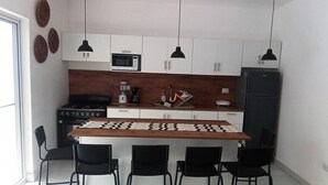 A modern kitchen with white cabinets, a black refrigerator, a microwave, a stove, and a coffee maker. There are four black chairs around a wooden table with a black and white pattern. - Sosua Villa Retreat - Calle Pedro Clisante (Sosúa)