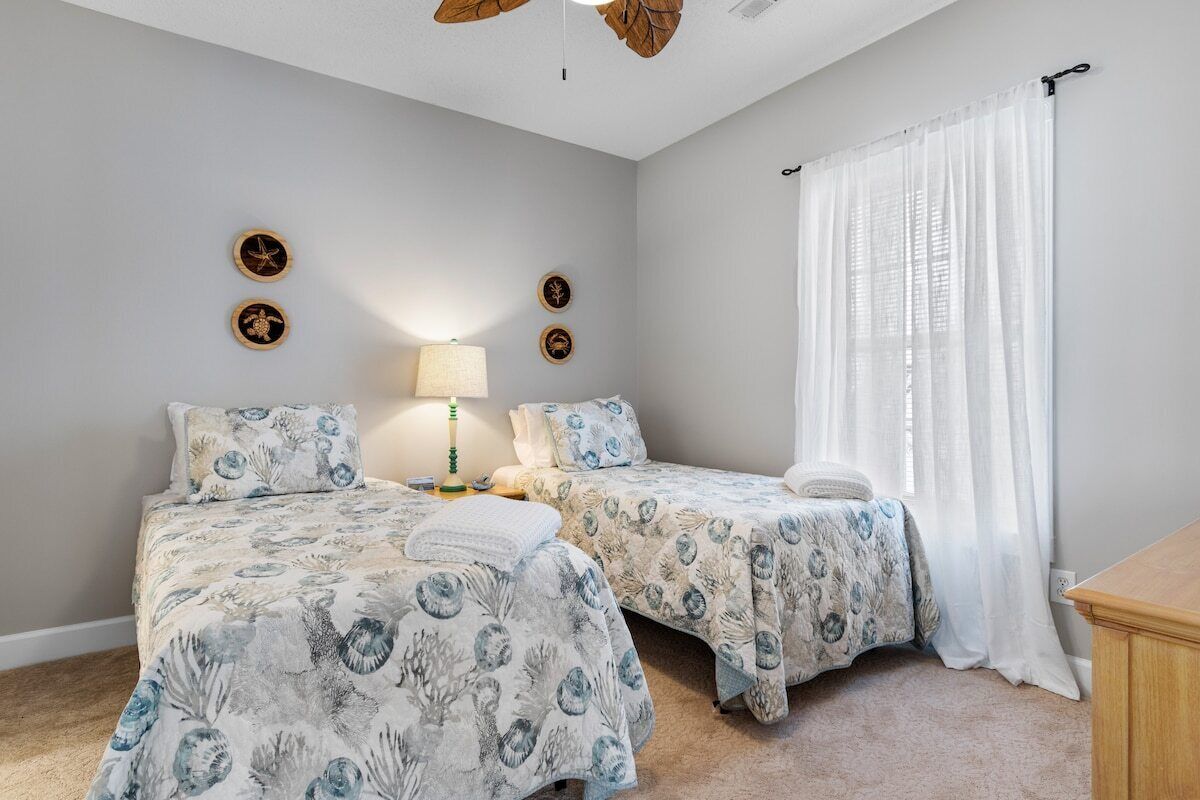 A bedroom with two beds, a nightstand, a lamp, and a ceiling fan.