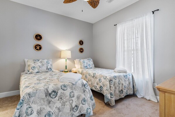 A bedroom with two beds, a nightstand, a lamp, and a ceiling fan.