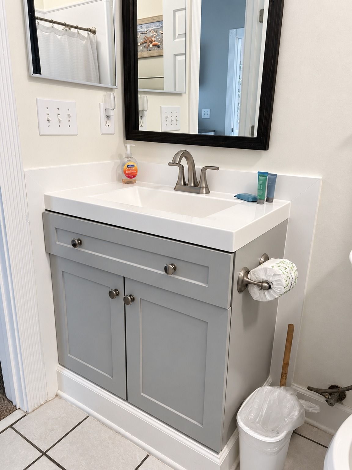 A bathroom with a white sink, grey cabinets, a mirror, and a toilet.