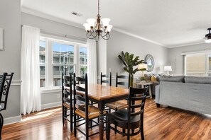 A dining area with a wooden table and chairs, a chandelier, and a view of the outside through large windows.