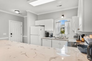 Une cuisine moderne avec des meubles blancs, un plan de travail en marbre et un four encastré.