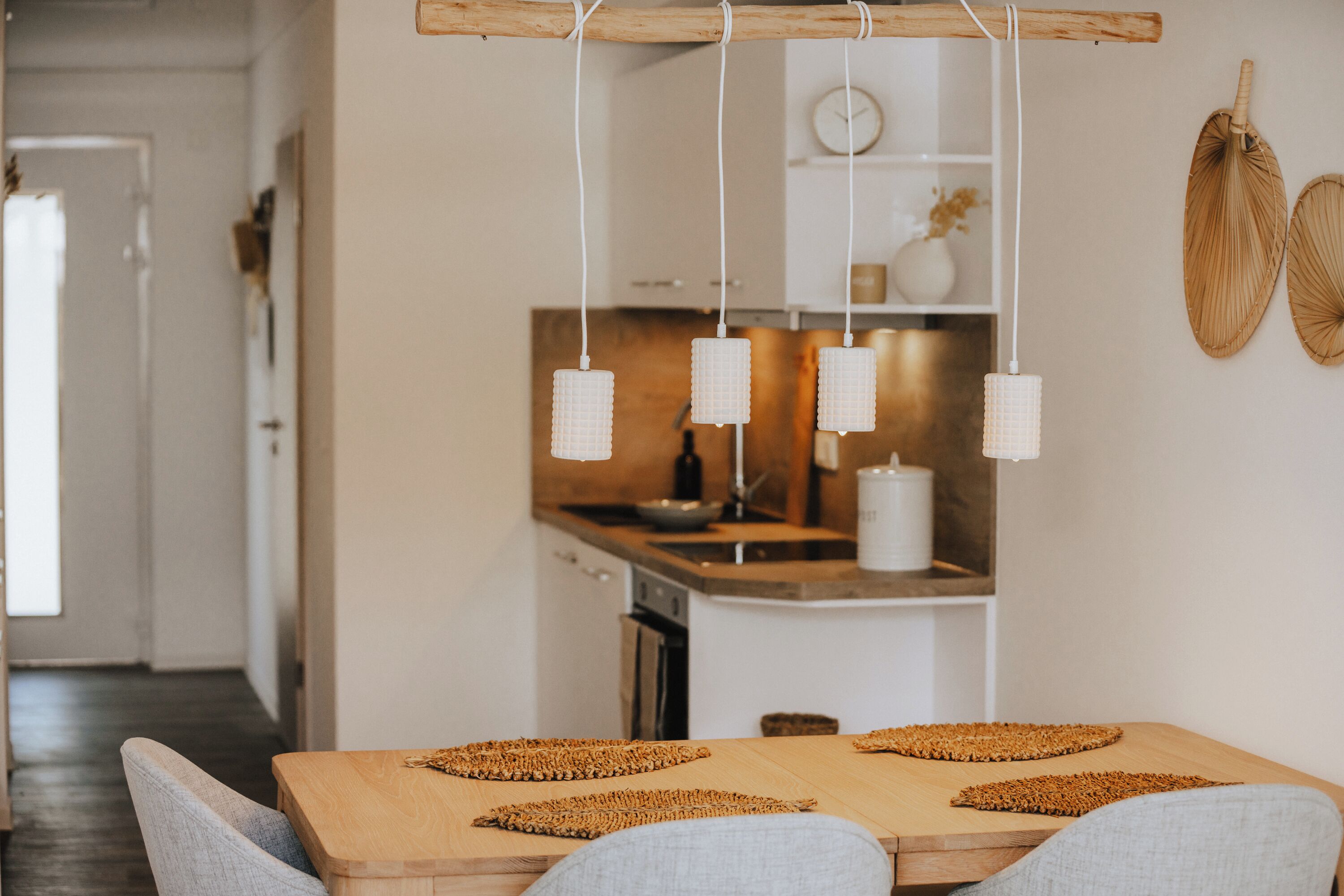 A modern kitchen with wooden countertops, hanging pendant lights, and woven placemats on the dining table.