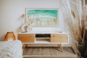 A white console bed with wooden drawers, a framed artwork titled "Boho - Beachhouse" by Forde Träutein, and a vase with dried plants.