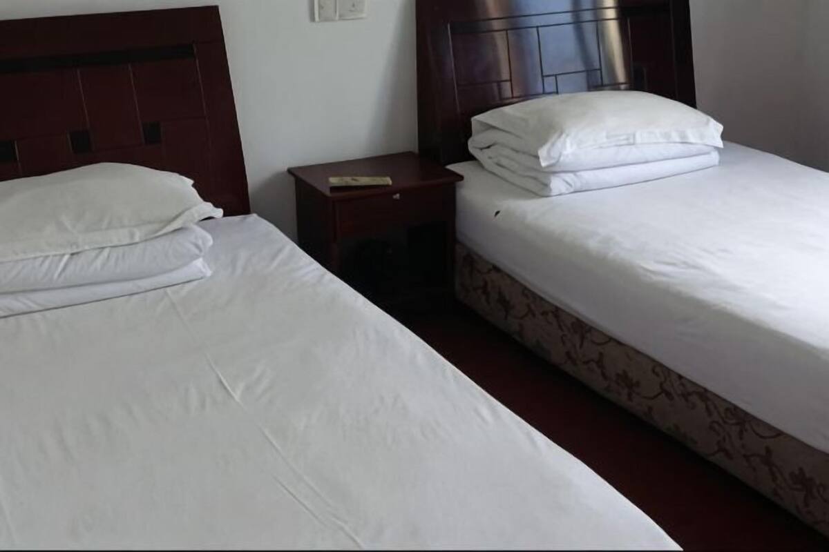 Dos camas con sábanas blancas, cabecero de madera, mesita de noche con un libro y falda de cama estampada.