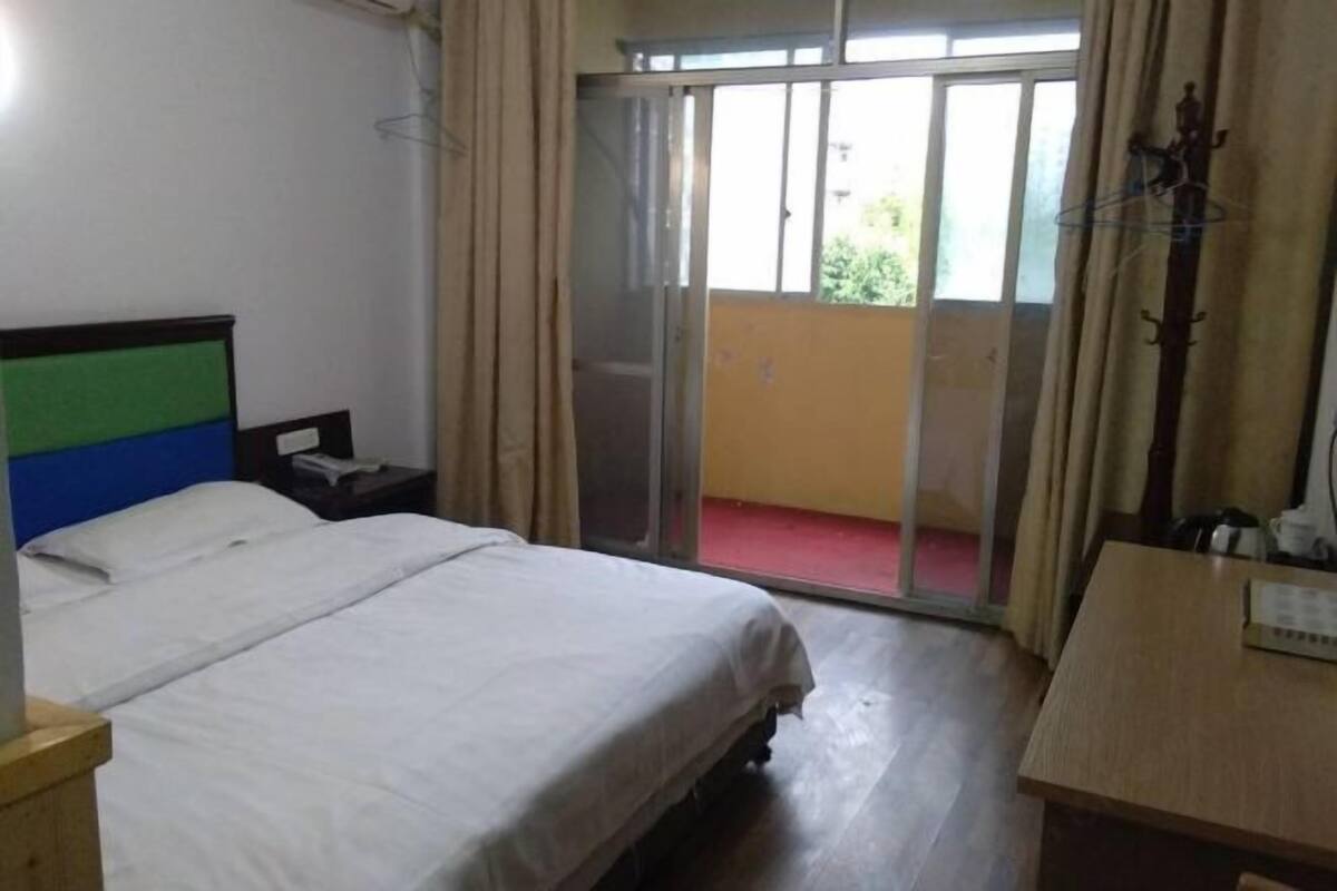 Habitación de hotel con cama, mesita de noche, escritorio y puerta corrediza de vidrio a un balcón.